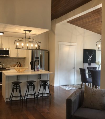 Remodeled Island style kitchen with a beautiful chandelier. White cabinets with black chairs and warm yellow lighting